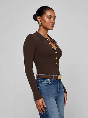 A woman with pulled-back hair wears the fitted Elisabetta Knit Bodysuit in chocolate brown, styled with blue jeans, a brown belt with a gold buckle, and gold hoop earrings, against a plain light gray background.