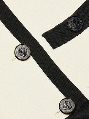 Close-up of the Janu Cropped Knit Jacket, a cream-colored knit with vintage sophistication, featuring a black stripe, three crested black buttons, and a partially visible pocket trimmed in black in the upper right corner.