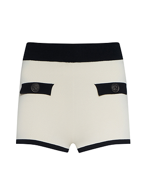 The Lumi Knit Micro Short is a white, high-waisted power knit short with a black waistband and hem, plus two front decorative pockets with black flaps and silver buttons—perfect for standing out at Spring 2026 NYFW.