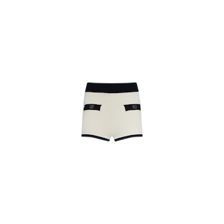 The Lumi Knit Micro Short showcases a white high-waisted silhouette with a contrasting black waistband and trim, meticulously crafted from sleek power knit. Designed with two front pockets accented by black flaps and round decorative emblems, these shorts embody the modern spirit of NYFW Spring 2026, presented on a plain white background.
