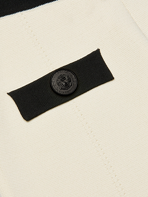Close-up of cream power knit fabric with a black horizontal band and round crest-embossed button—a chic detail from the Lumi Knit Micro Short, featured at Spring 2026 NYFW.