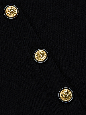 Close-up of the Ronda Knit Henley Top by L'AGENCE: black fabric with three gold lion head buttons featuring a decorative pattern and thin silver borders, offering bold contrast on this chic piece.