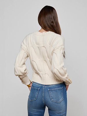 A woman with long brown hair, seen from behind, wears the L'AGENCE Storm Cable-Knit Sweater in cream with gold buttons and blue jeans, standing against a plain light gray background.