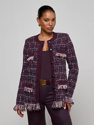 A woman wears the L’AGENCE Kastoria Fringe Cardigan, a maroon and pink boucle tweed longline jacket with fringe details, over matching maroon top and pants, standing against a light gray background.