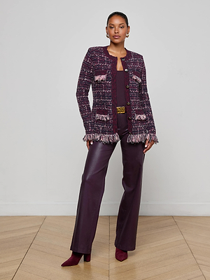 A woman stands on a wooden floor wearing the L'AGENCE Kastoria Fringe Cardigan in burgundy, paired with a matching top, wide-leg pants, and pointed toe heels. She accessorizes with hoop earrings and poses confidently against a plain background.