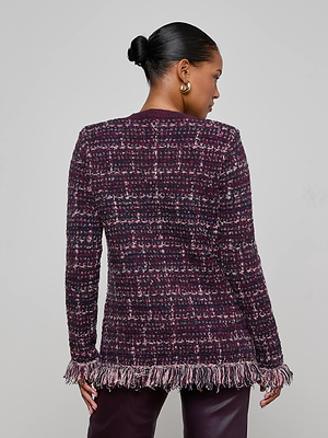 A woman with her hair in a low bun models the L'AGENCE Kastoria Fringe Cardigan, featuring textured boucle tweed and fringe at the hem and cuffs, as she faces away from the camera against a plain light gray background.