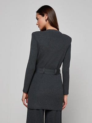 A woman with long brown hair stands with her back to the camera, wearing the dark gray Lore Cardigan with a tie belt and matching pants, set against a plain light background.