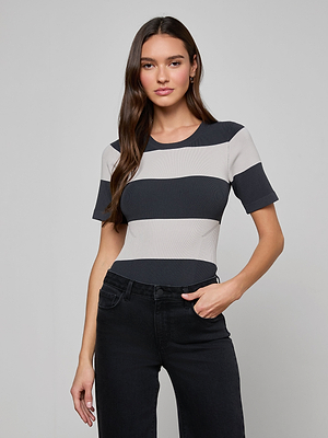 A woman with long brown hair wears the Rosemond Bodysuit and black jeans, standing against a plain light gray background with one hand in her pocket and a neutral expression.