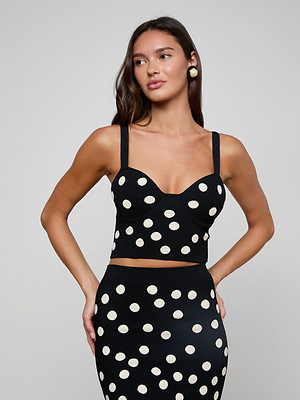 A woman in the Tula Knit Bra Top and a matching high-waisted black skirt with white polka dots stands against a plain light gray background.