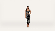 A woman stands against a plain white background, wearing a black crop top and matching midi skirt with white polka dots, and black high-heeled sandals.
