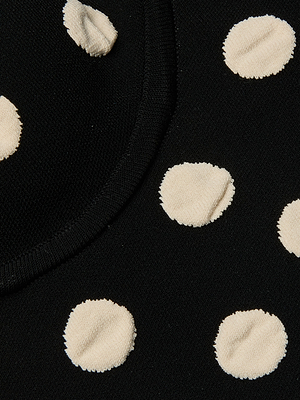 Close-up of the Tula Knit Bra Tops black compression knit fabric featuring evenly spaced raised jacquard polka dots and a curved seam across the upper left corner.