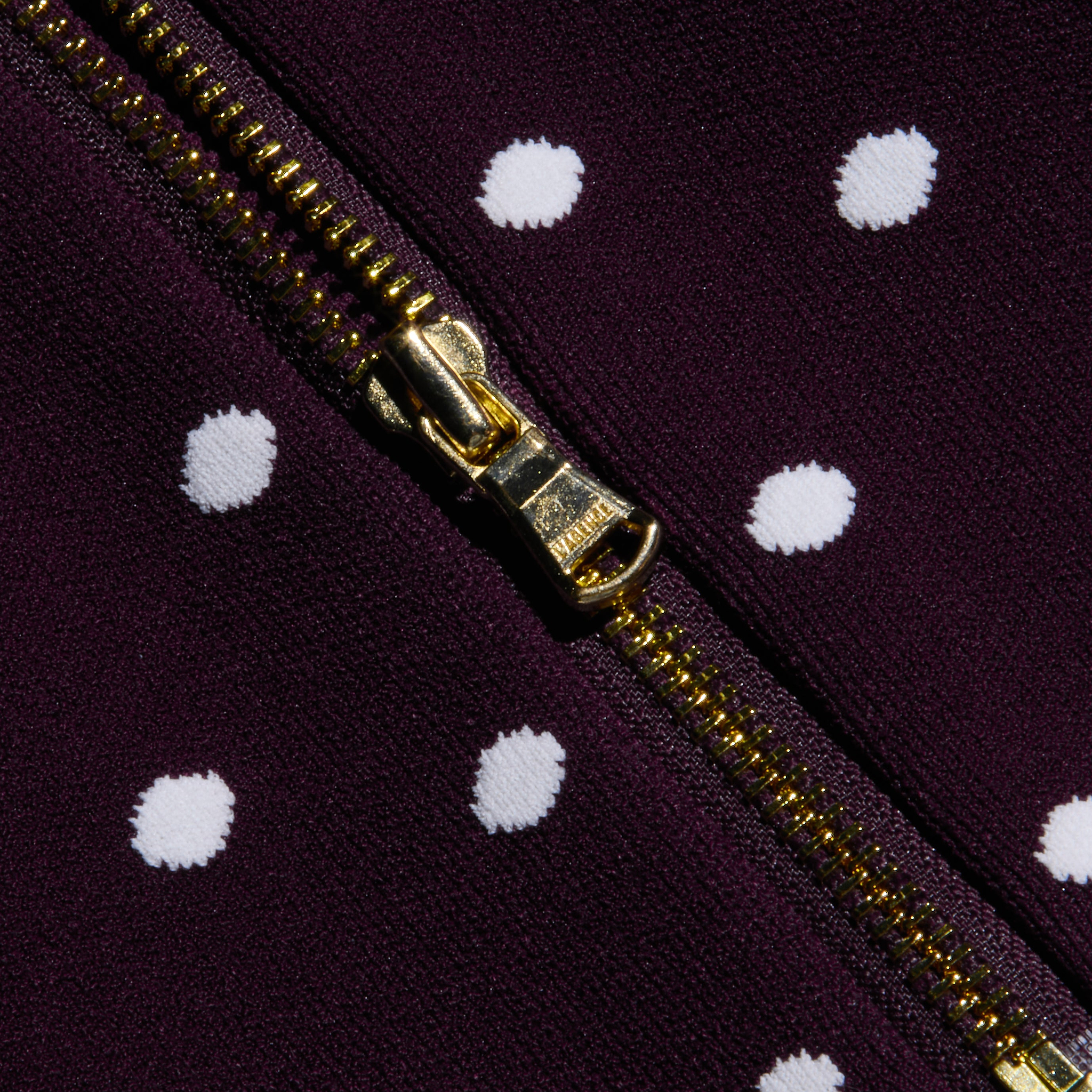 A close-up of the Tula Knit Bra Top’s gold zipper on dark purple fabric featuring evenly spaced white jacquard polka dots.