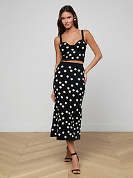 A woman poses against a plain white background wearing the Mae Knit Flare Skirt, a black skirt with large white polka dots, paired with a matching crop top and black strappy heels.