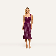A woman stands facing forward against a plain background, wearing the Mae Knit Flare Skirt — a sleeveless, fitted purple dress with white polka dots and a flared hem that creates a flattering silhouette. She has blonde hair and is paired with open-toed heels.