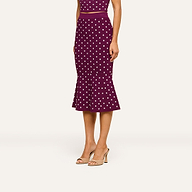 A woman stands in nude high-heeled sandals against a plain light background, wearing the Mae Knit Flare Skirt styled as a purple, sleeveless, polka-dot dress with a flared hem reminiscent of a fit and flare silhouette. Her face is not visible.