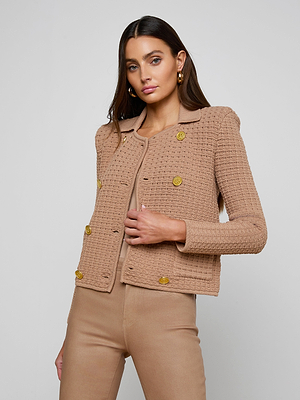 A woman with long brown hair wears the Charlie Knit Jacket, a tailored tan button-up style with gold buttons and matching tan pants, standing against a plain light gray background.