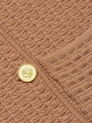 A close-up of the Charlie Knit Jacket, a textured brown knit style with a gold lion-embossed button and decorative details.