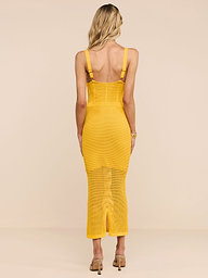 Una donna dai capelli biondi indossa labito in maglia Michelle di colore giallo e sandali con tacco beige, in piedi di spalle alla fotocamera su uno sfondo beige a tinta unita.