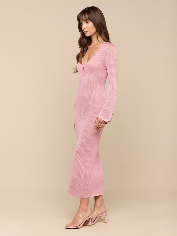 A woman in a fitted, long-sleeve pink Sydney Knit Dress and heeled sandals stands against a plain white background, posed in profile with her arms relaxed by her sides.