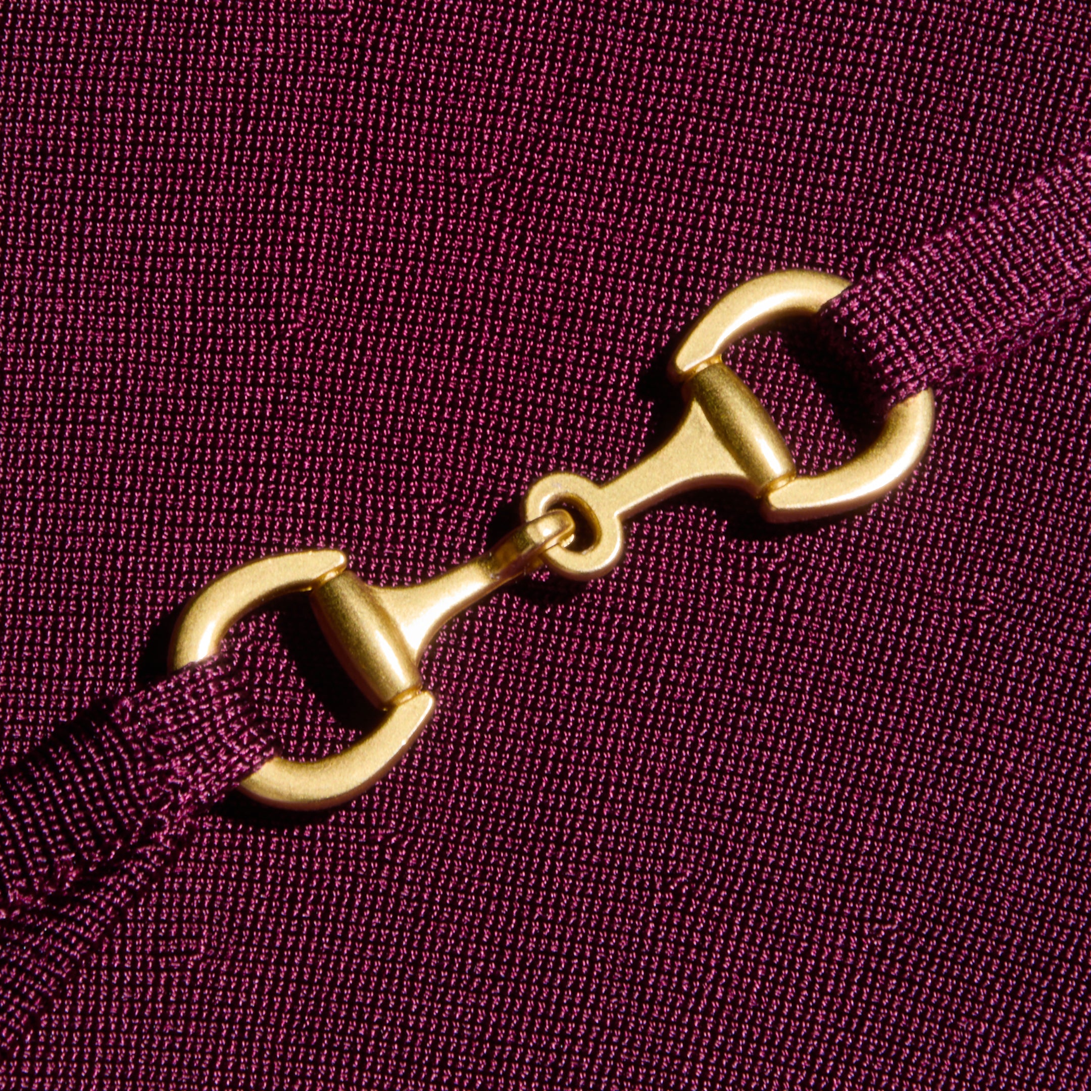 A close-up of a gold metal clasp connecting two ends of an adjustable purple strap, set against the textured stretch knit fabric of the Lana Flare Knit Dress.