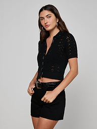 Wearing the Ninette Knit Top—a black short-sleeve, button-up crochet design with grosgrain ribbon trim—a woman poses with black belted shorts against a plain, light background.