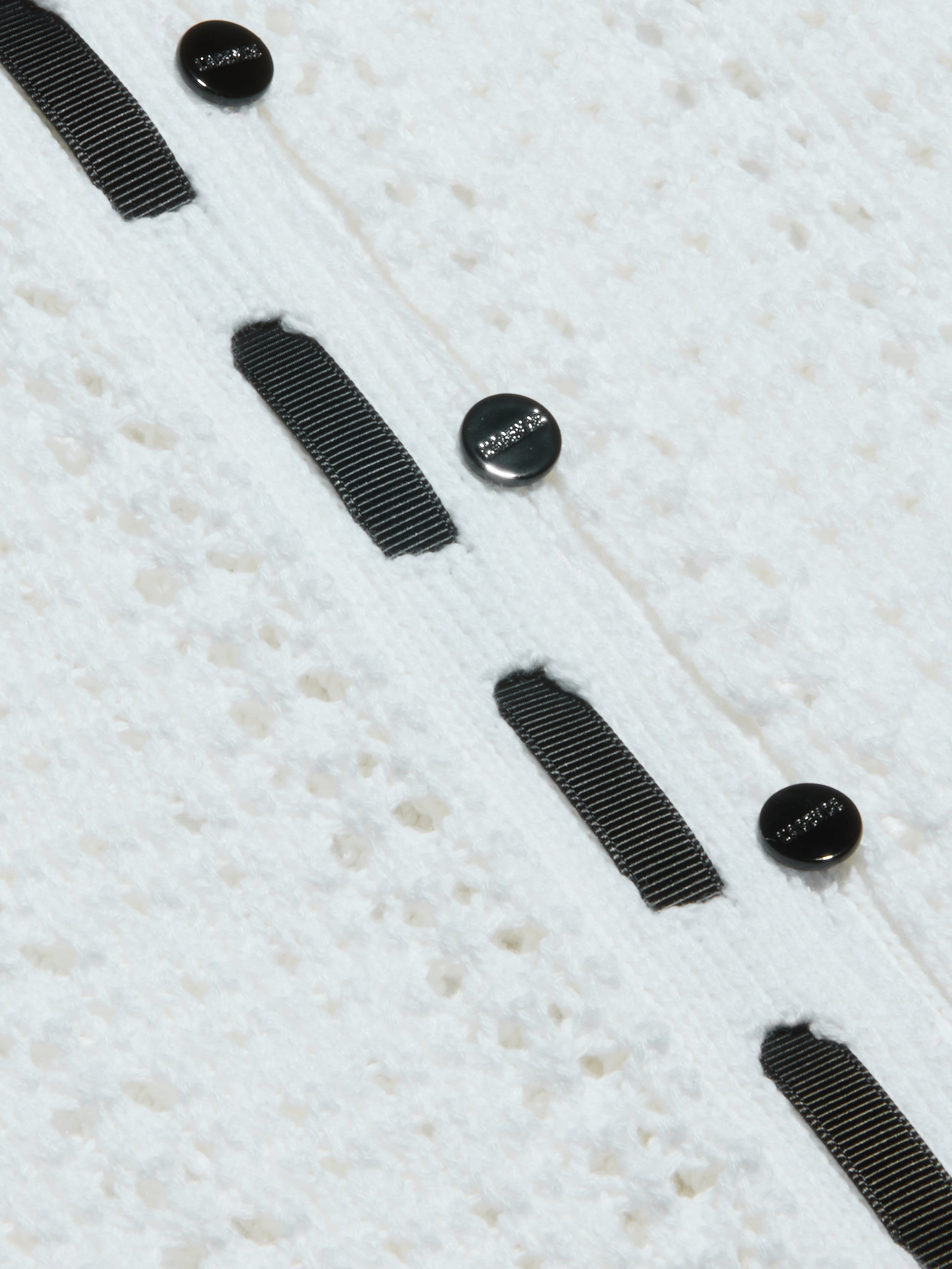 Close-up of the Ninette Knit Top, featuring textured white fabric, three black round buttons, and parallel grosgrain ribbon trims stitched vertically for a touch of Parisian flair.