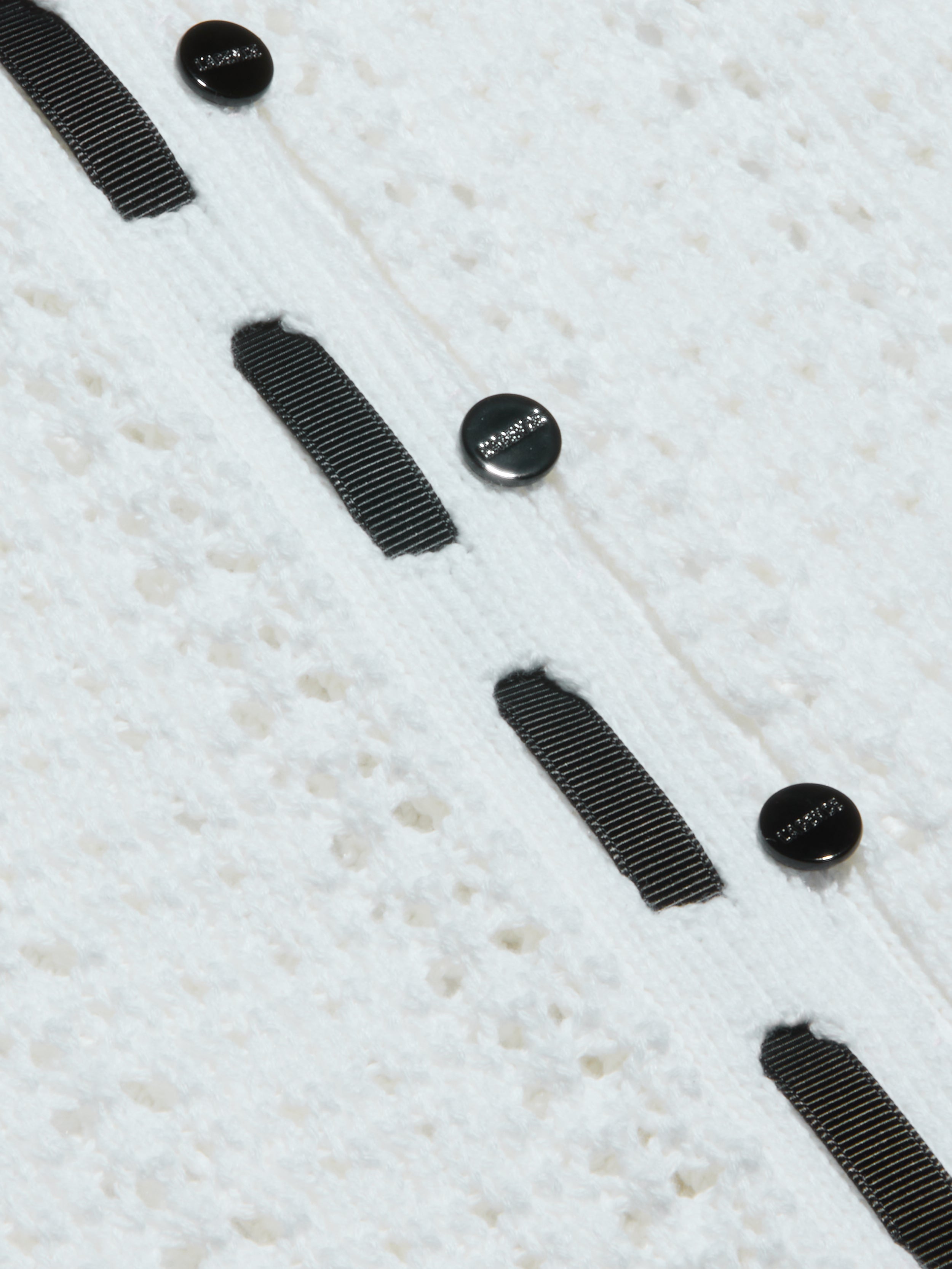 Close-up of the Ninette Knit Top, featuring textured white fabric, three black round buttons, and parallel grosgrain ribbon trims stitched vertically for a touch of Parisian flair.