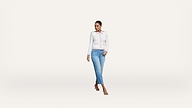 A woman wearing a white jacket, light pink shirt, blue jeans, and heels walks confidently against a plain white background.
