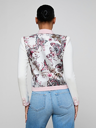 A woman with her hair in a bun is shown from the back against a plain light background, wearing the Nomi Satin Back Cardigan featuring statement buttons and white sleeves, paired with light blue jeans.