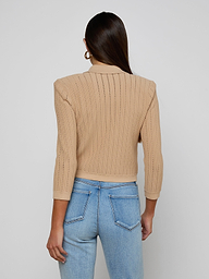 A woman with long brown hair, wearing the Risa Collared Cardigan in beige and light blue jeans, stands facing away from the camera against a plain light background.