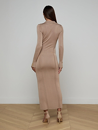 A woman stands facing away against a plain white background, her straight brown hair flowing down her back as she models the Delma Knit Maxi Dress—a long-sleeved, fitted knit blend—paired with beige heels.