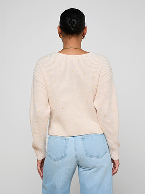 A person with dark hair in a neat bun is shown from behind, wearing the Antonella Crossover Sweater in light pink and light blue high-waisted jeans against a plain background.