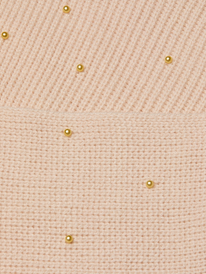 The Antonella Crossover Sweater features a light pink knit with ribbed detailing on top and plain knit below, adorned with small gold beads for a delicate, pearl-accented look.