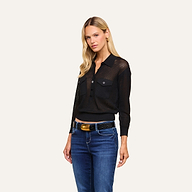 A woman with long blonde hair wears the black Carine Top, a lightweight knit design featuring a button placket, paired with blue jeans. She stands facing forward with a neutral expression against a plain light background.