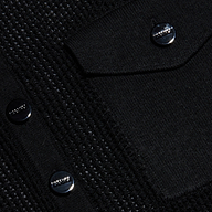 Close-up of the Carine Top’s textured black fabric, featuring shiny black buttons with a row of small raised metallic studs and a flap pocket. The surface combines lightweight knit textures with smooth patterns for added visual interest.