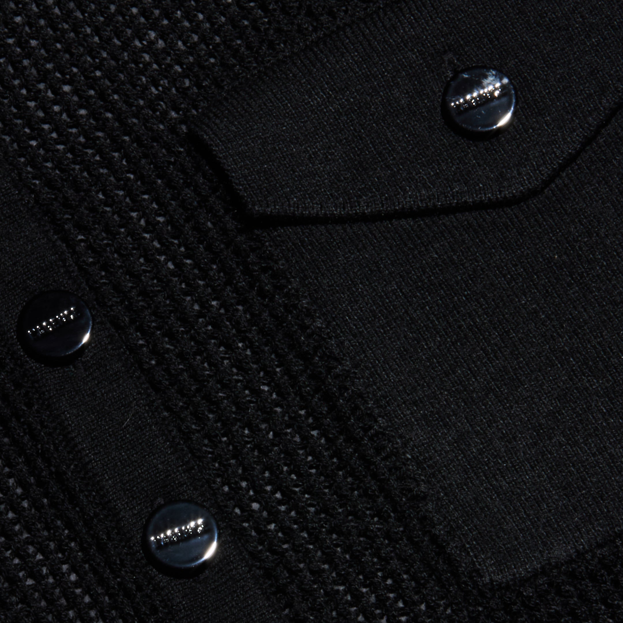 Close-up of the Carine Top’s textured black fabric, featuring shiny black buttons with a row of small raised metallic studs and a flap pocket. The surface combines lightweight knit textures with smooth patterns for added visual interest.