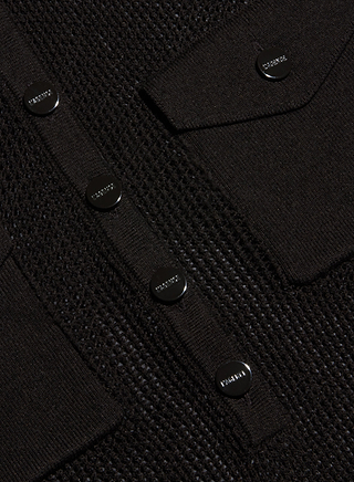 Close-up of the Carine Top—a black textured knit cardigan crafted in a lightweight fabric with shiny black buttons and two flap pockets, each button engraved with the Prada logo. This chic detail evokes styles inspired by New York Fashion Week.