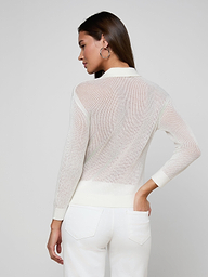 A woman stands with her back to the camera, wearing a sheer white long-sleeve Carine Top and white utility pocket jeans, one hand on her hip, against a plain light background.