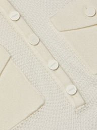 Close-up of the Carine Top, featuring a cream-colored textured lightweight knit, utility pockets, and a row of round white buttons engraved with LAGERFELD.