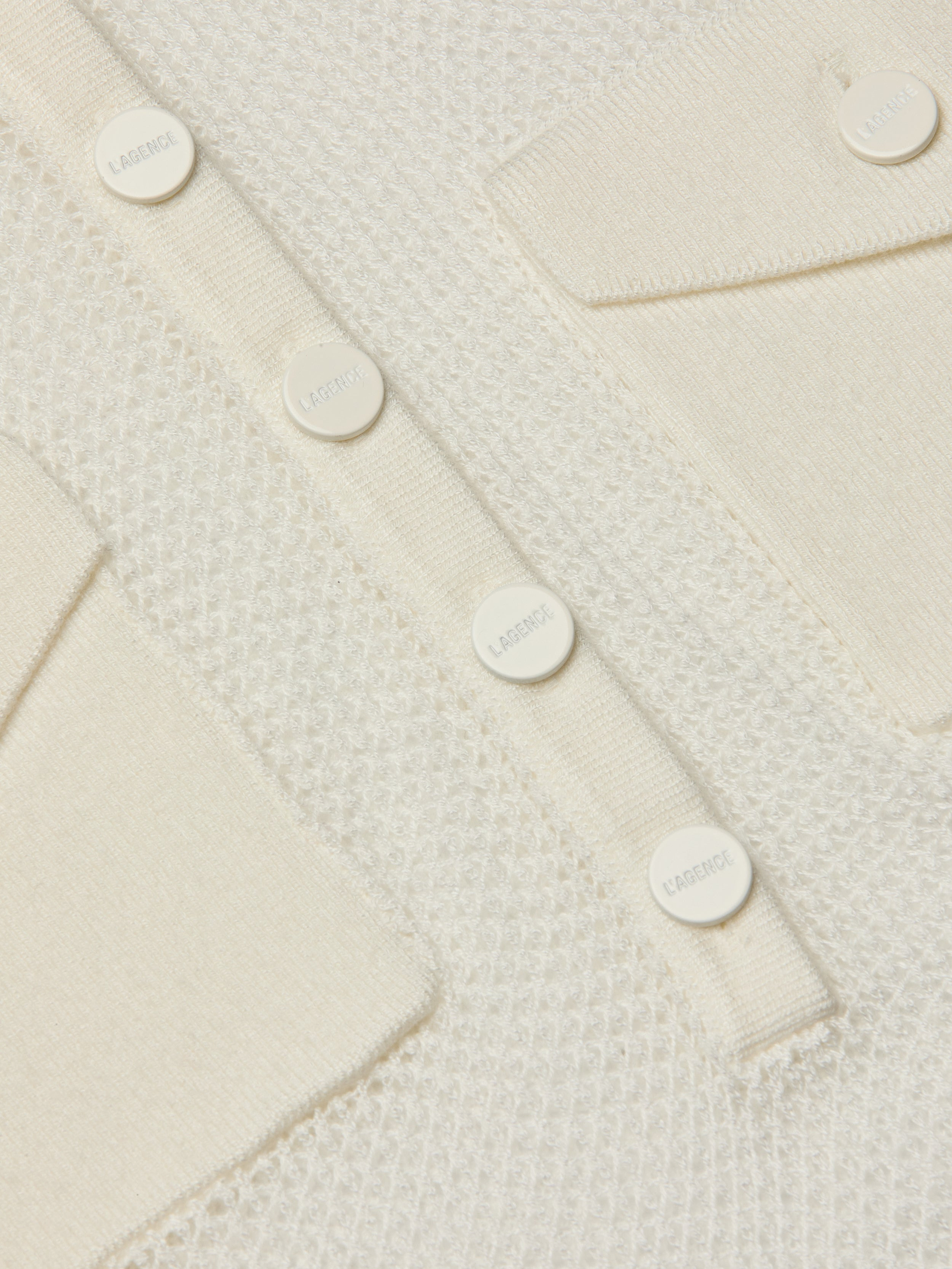 Close-up of the Carine Top, featuring a cream-colored textured lightweight knit, utility pockets, and a row of round white buttons engraved with LAGERFELD.