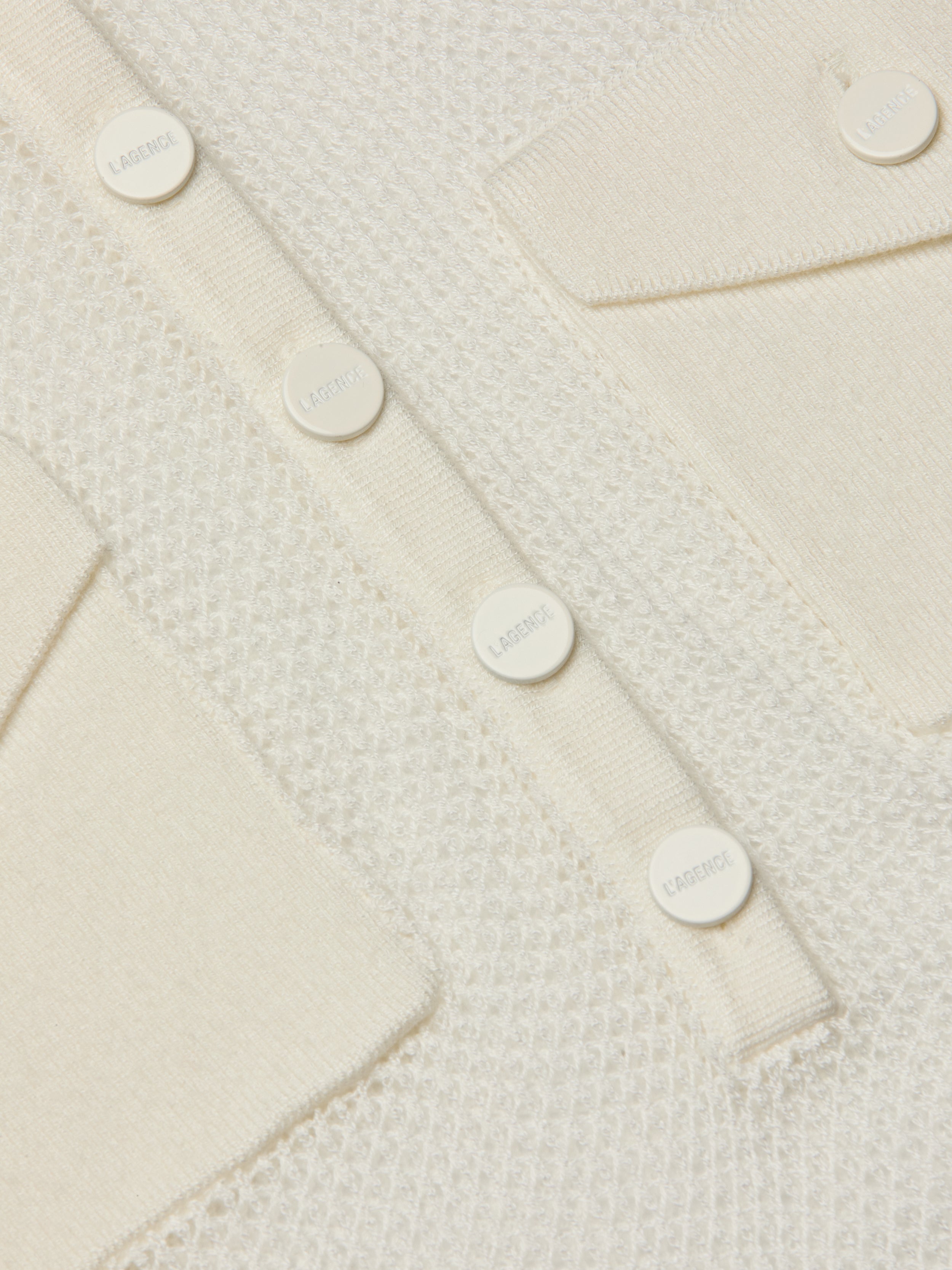 Close-up of the Carine Top, featuring a cream-colored textured lightweight knit, utility pockets, and a row of round white buttons engraved with LAGERFELD.