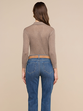 Une femme aux longs cheveux châtains se tient dos à la caméra ; elle porte le haut Carine ajusté, de couleur taupe, et un jean bleu, devant un fond beige uni.