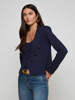 Woman with long dark hair wears the Mercer Knit Blazer over a matching top, blue jeans, and a gold belt. She stands against a plain light background, facing forward with one hand in her pocket.