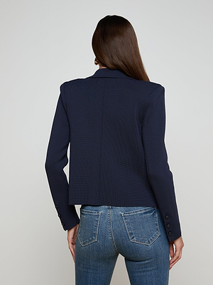 A person with long brown hair is seen from the back, wearing the Mercer Knit Blazer in navy blue and blue jeans against a plain light background.