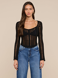 A woman with long brown hair wears the Orine Pointelle Knit Top in black, paired with blue jeans, standing against a plain light background.