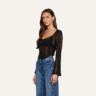 A woman wearing the Orine Pointelle Knit Top in black, featuring long sleeves and a scoop neckline, paired with blue jeans and standing against a plain off-white background.