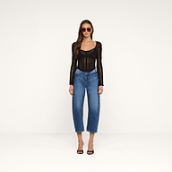 A woman wearing sunglasses, the Orine Pointelle Knit Top with bell sleeves, blue high-waisted jeans, and black open-toe heels stands against a plain white background.