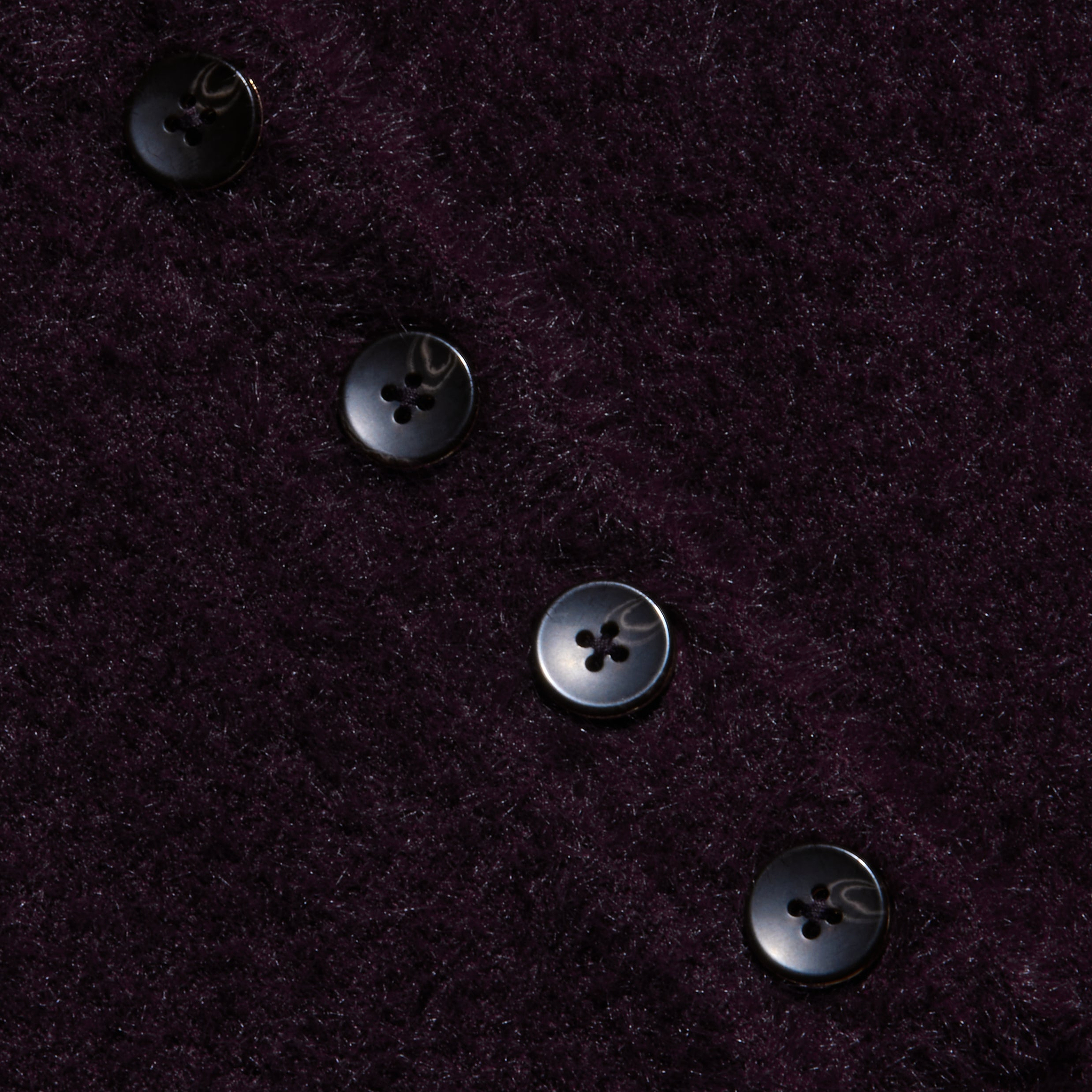 Four black buttons in a diagonal line accent the plush, dark purple knit of the Cirrus Cropped Polo, resting on its textured, fuzzy fabric background.