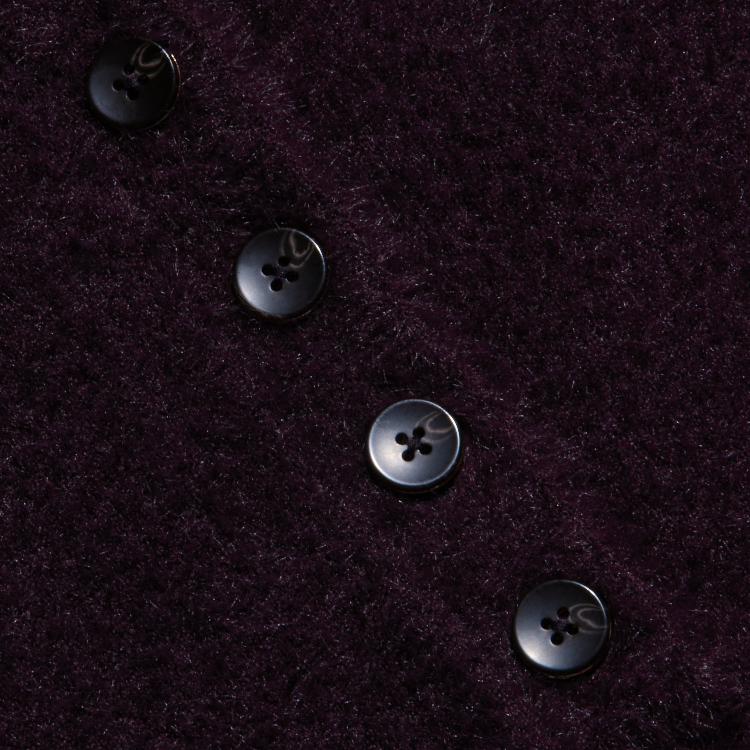 Four black buttons in a diagonal line accent the plush, dark purple knit of the Cirrus Cropped Polo, resting on its textured, fuzzy fabric background.