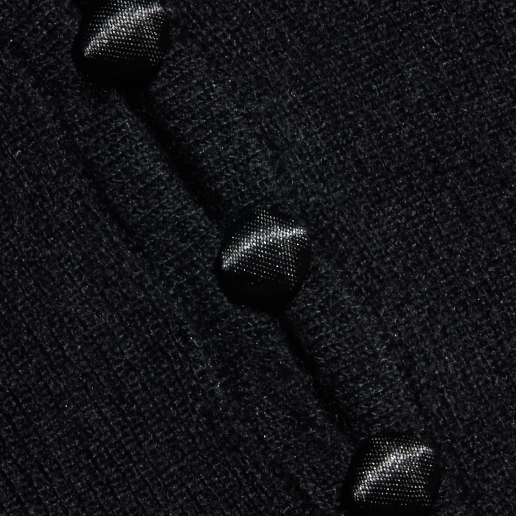 Close-up of the Eluna Cardigan Top’s textured black wool-blend fabric, featuring three glossy black buttons sewn in a diagonal line.